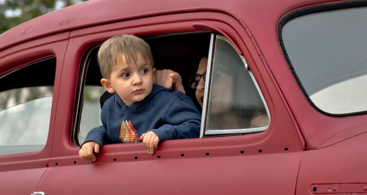 A child sticks his head out of a red car