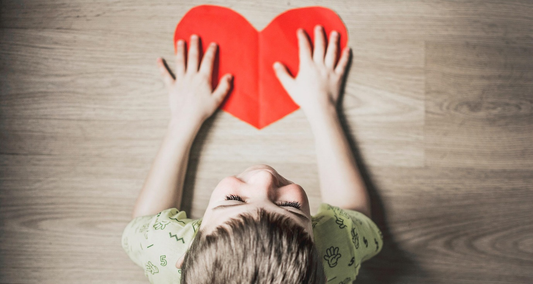 A child holding a heart made of red paper