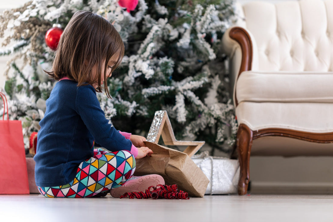 A girl is opening the gift in front of the Christmas tree